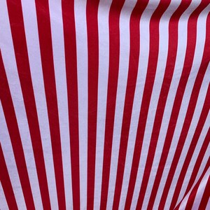 May include: Red and white striped fabric with a subtle sheen. The fabric is folded and draped, creating a wave-like pattern.