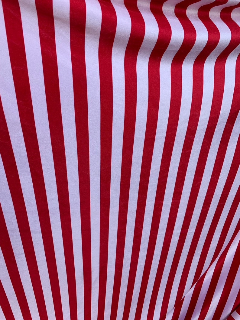 May include: Red and white striped fabric with a subtle sheen. The fabric is folded and draped, creating a wave-like pattern.