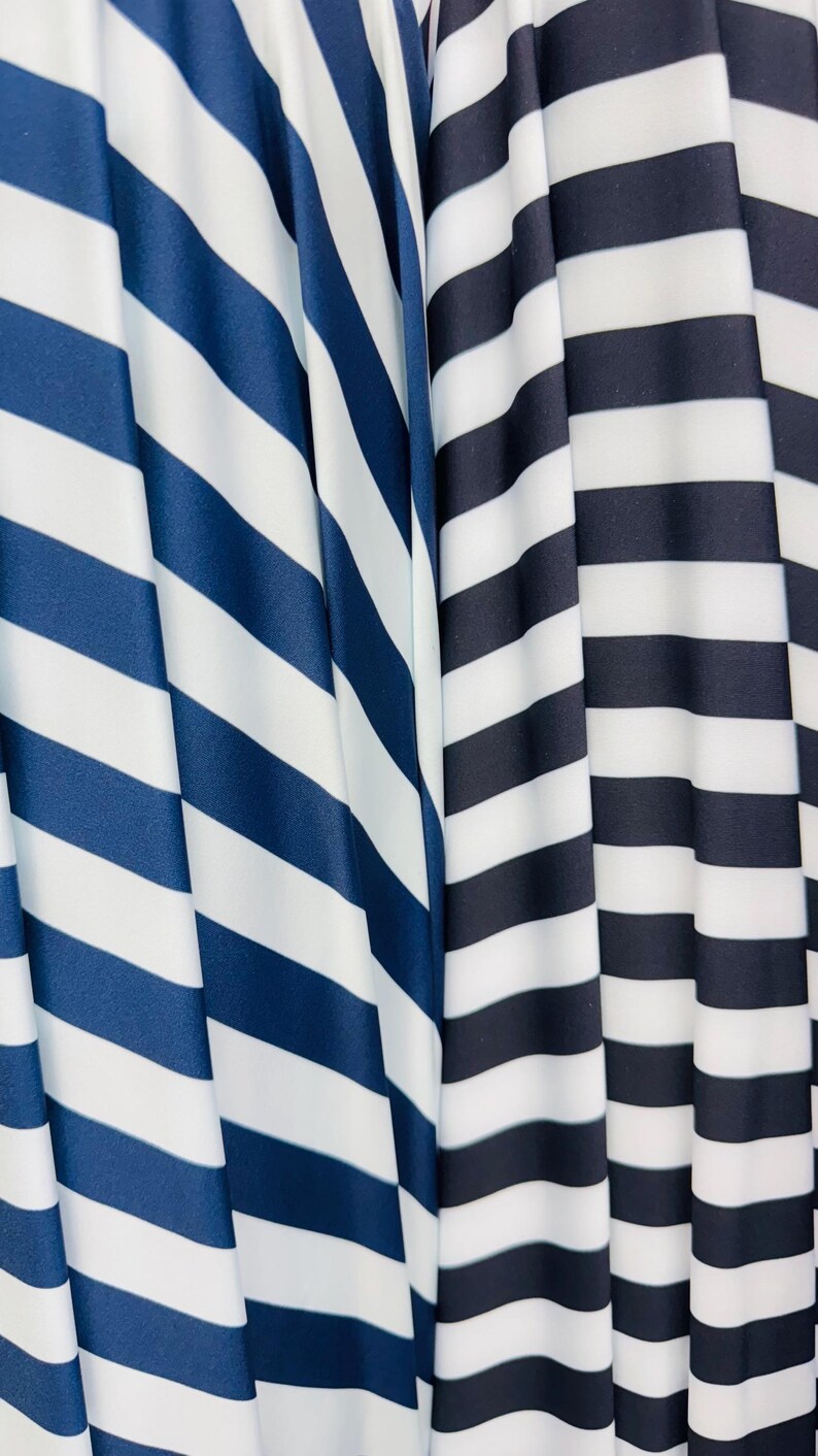 K&ouml;nnte beinhalten: Nahaufnahme von zwei Stoffen mit kr&auml;ftigen, diagonalen Streifen. Ein Stoff hat marineblaue und wei&szlig;e Streifen, w&auml;hrend der andere schwarz-wei&szlig;e Streifen aufweist. Die Stoffe sind drapiert und erzeugen weiche Falten und Schatten.