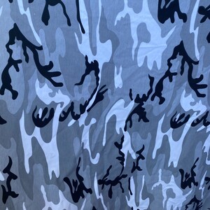 May include: A close-up of a fabric with a camouflage pattern in shades of grey and black.