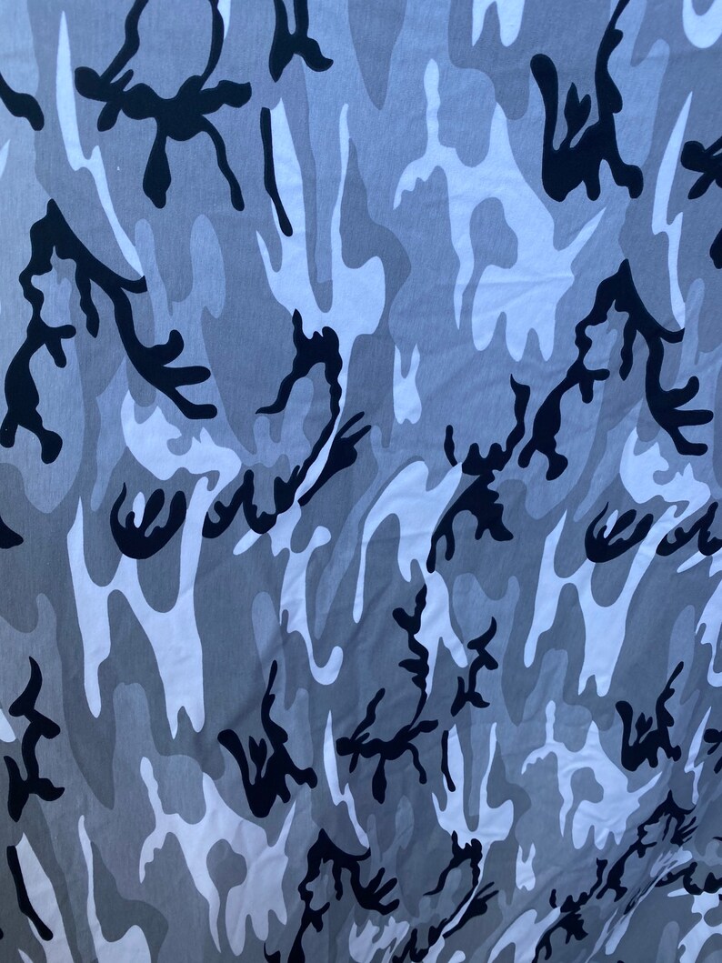 May include: A close-up of a fabric with a camouflage pattern in shades of grey and black.