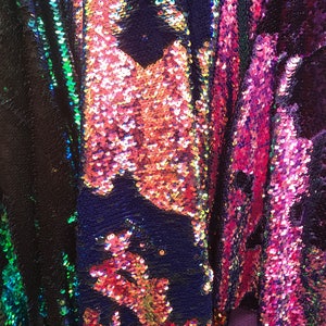 Può includere: Primo piano di un tessuto iridescente con paillettes in tonalità rosa, verde e blu. Le paillettes sono disposte in un motivo a strisce verticali.