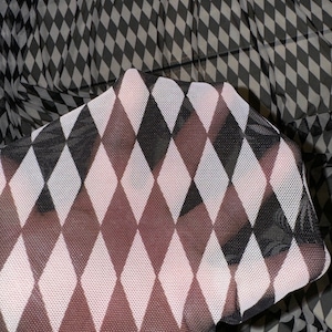 May include: A white and black harlequin patterned sheer fabric with a diamond pattern. The fabric is translucent and has a delicate texture.