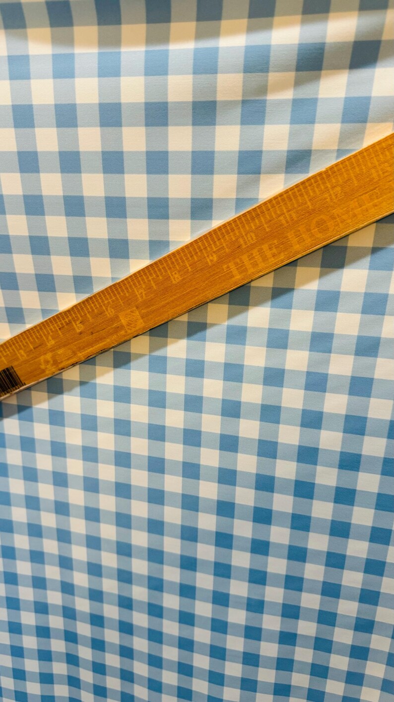 K&ouml;nnte beinhalten: Blau-wei&szlig;es Gingham-Gewebe mit einem Holzlineal darauf. Das Lineal ist in Zoll eingeteilt.