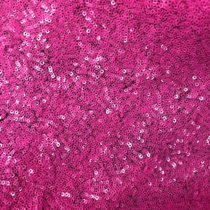 May include: A close-up of a fabric covered in pink sequins. The sequins are small and tightly packed together, creating a shimmering effect.