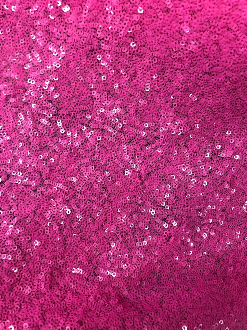 May include: A close-up of a fabric covered in pink sequins. The sequins are small and tightly packed together, creating a shimmering effect.