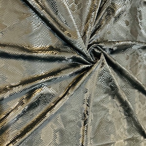 Könnte beinhalten: Schwarzer Stoff mit Schlangenhautmuster. Der Stoff ist zerknittert und hat eine glänzende Oberfläche.