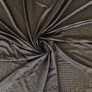 Op de afbeelding: Een donkerbruine stof met een dicht, uniform patroon van kleine, reflecterende, ronde studs gerangschikt in een raster. Het materiaal is in het midden samengebracht, waardoor stralende plooien en draperingen ontstaan die de textuur benadrukken.