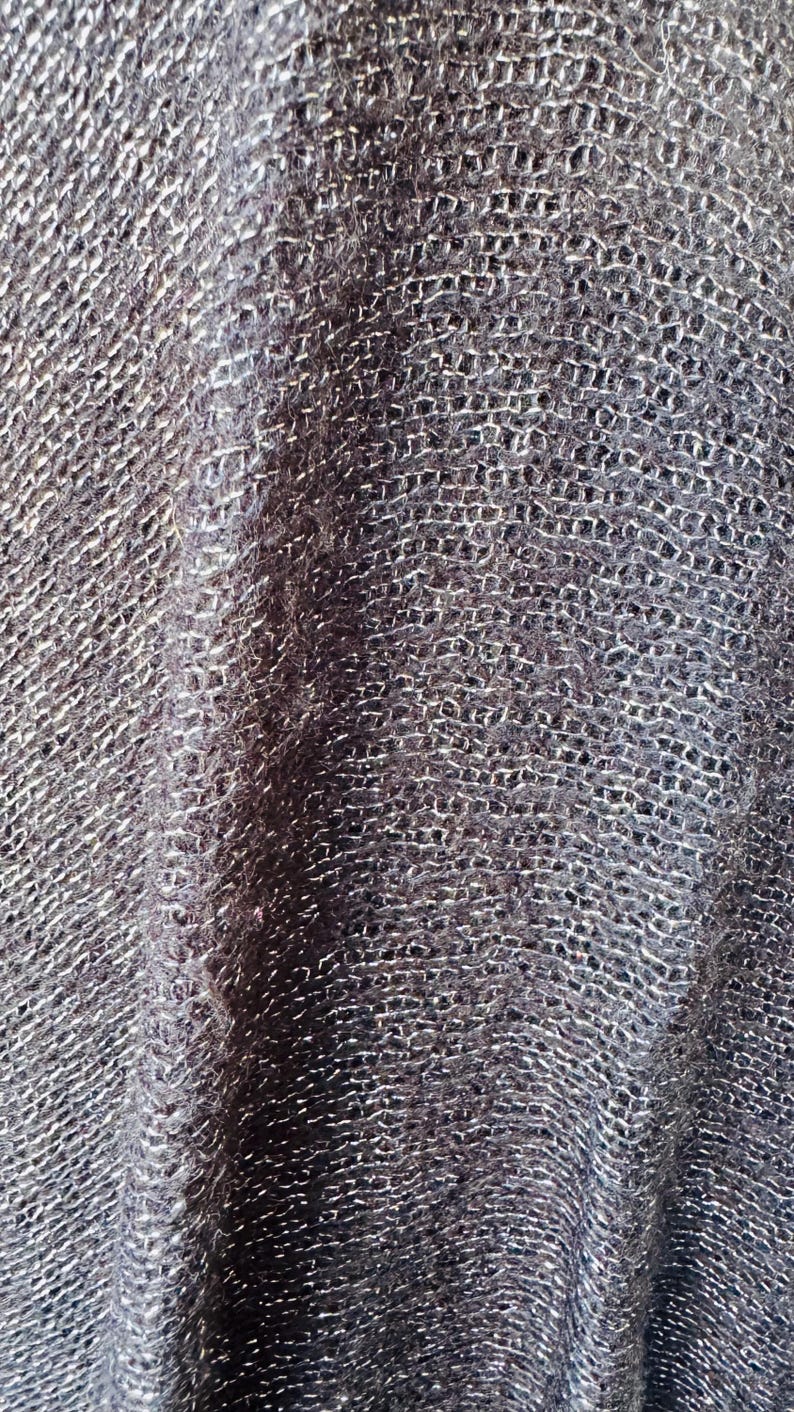 Puede incluir: Primer plano de una tela de punto gris oscuro con un brillo sutil. La tela tiene un patr&oacute;n tejido texturizado.
