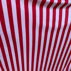 May include: Red and white striped fabric with a subtle sheen. The fabric is folded and draped, creating a wave-like pattern.