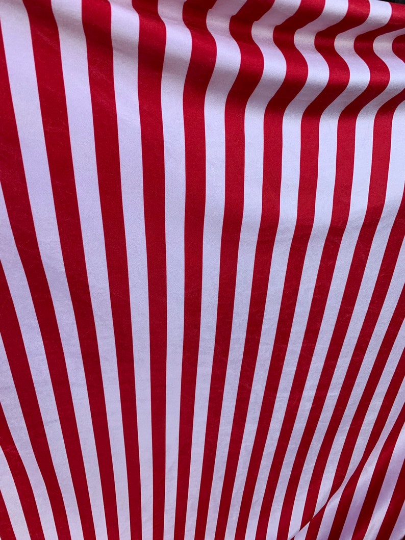 May include: Red and white striped fabric with a subtle sheen. The fabric is folded and draped, creating a wave-like pattern.