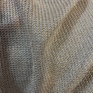 Puede incluir: Primer plano de una tela de punto beige con un acabado brillante. La tela tiene un tejido suelto y abierto y una superficie ligeramente texturizada.