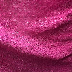 May include: Close-up of a pink fabric with sequins. The sequins are small and tightly packed together, creating a shimmering effect.