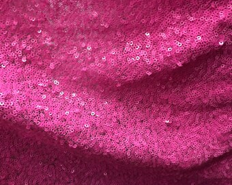 May include: Close-up of a pink fabric with sequins. The sequins are small and tightly packed together, creating a shimmering effect.