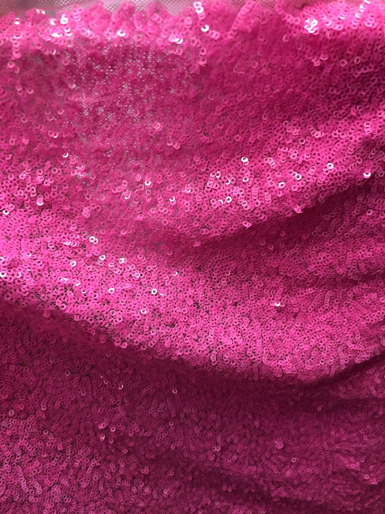 May include: Close-up of a pink fabric with sequins. The sequins are small and tightly packed together, creating a shimmering effect.