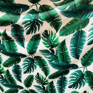 Op de afbeelding: Een witte stof met een herhalend patroon van groene tropische bladeren. De bladeren zijn in verschillende vormen en maten, waaronder palmbladeren en monstera bladeren.