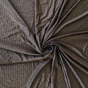 Op de afbeelding: Een donkerbruine stof met een herhalend patroon van kleine, verhoogde, cirkelvormige stippen in een raster. Het materiaal is in een centrale spiraal gedrapeerd, wat diepe plooien en schaduwen cre&euml;ert die de textuur van het oppervlak benadrukken.