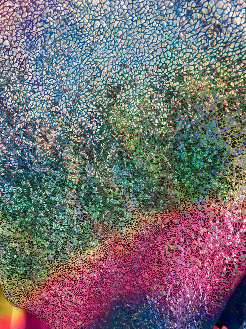 K&ouml;nnte beinhalten: Ein regenbogenfarbener, irisierender Stoff mit einem Rissmuster aus Glas. Der Stoff ist ein Farbverlauf von Blau, Gr&uuml;n, Gelb, Orange, Rosa und Lila.