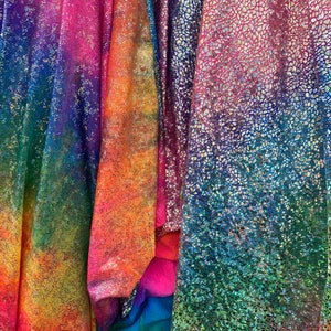 K&ouml;nnte beinhalten: Vier verschiedene irisierende Stoffe mit einem Regenbogen-Farbmuster. Die Stoffe haben eine strukturierte, glitzernde Oberfl&auml;che.