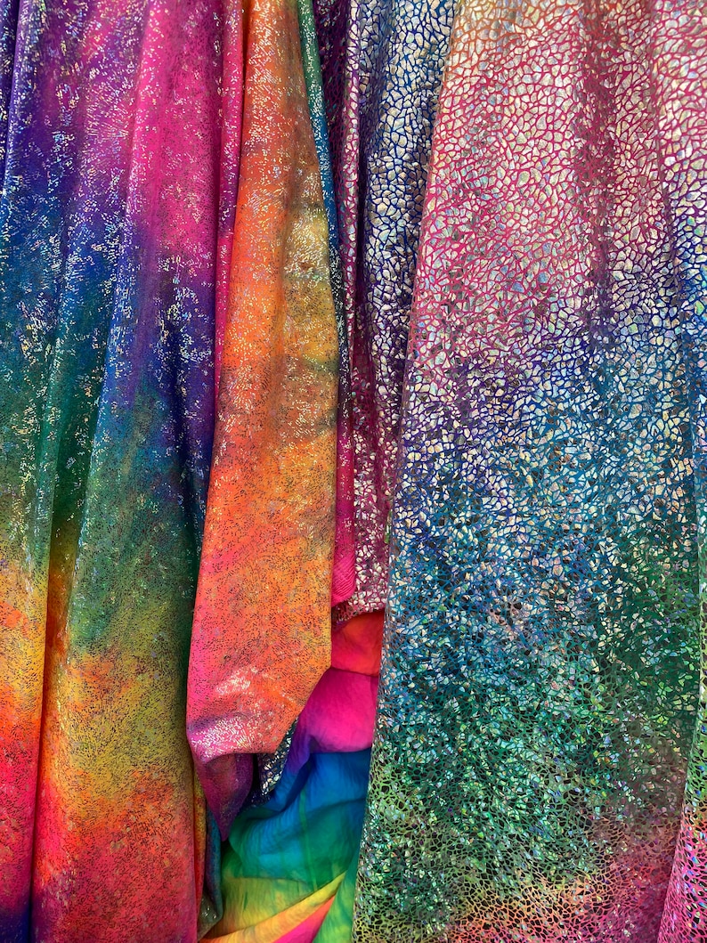 K&ouml;nnte beinhalten: Vier verschiedene irisierende Stoffe mit einem Regenbogen-Farbmuster. Die Stoffe haben eine strukturierte, glitzernde Oberfl&auml;che.