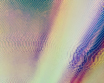 Op de afbeelding: Een close-up van een iriserende nep-slangenhuidstof met een textuurpatroon. De stof heeft een lichtblauwe, paarse en roze kleurstelling.