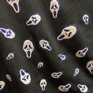May include: Black fabric with a repeating pattern of white ghost faces with blue glitter accents. The ghost faces are in a scream pose with their mouths open.