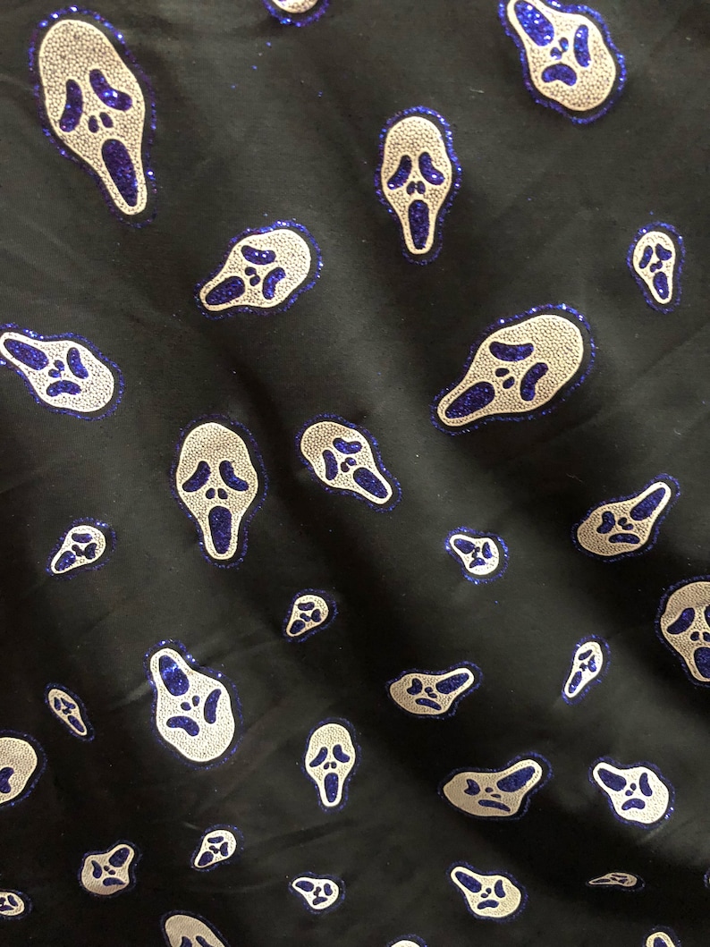 May include: Black fabric with a repeating pattern of white ghost faces with blue glitter accents. The ghost faces are in a scream pose with their mouths open.