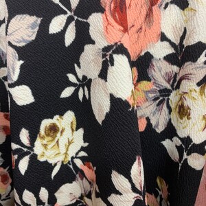 May include: Close-up of a black fabric with a floral pattern. The fabric features pink, white, and brown roses with green leaves.