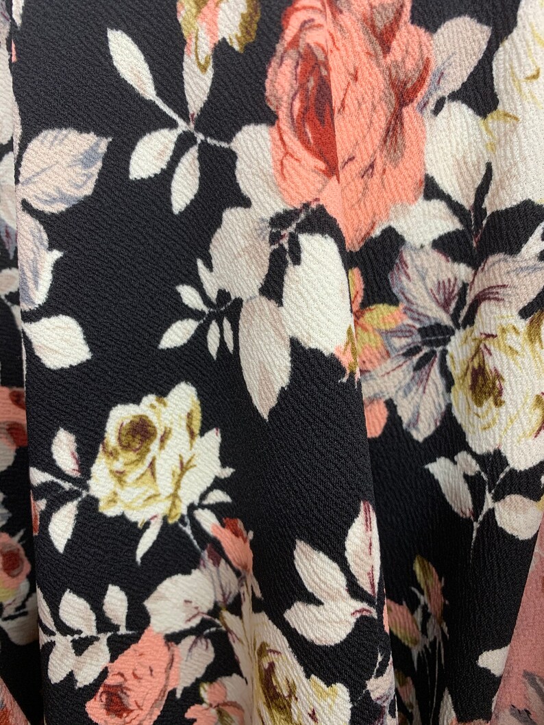 May include: Close-up of a black fabric with a floral pattern. The fabric features pink, white, and brown roses with green leaves.