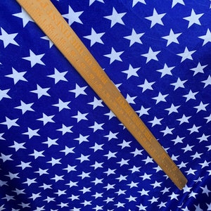 May include: Blue fabric with a white star pattern. The fabric is measured with a wooden ruler.