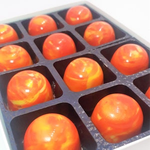 Puede incluir: Una caja de 10 chocolates de color naranja y amarillo en espiral dispuestos en forma de cuadr&iacute;cula. Los chocolates est&aacute;n en una caja blanca con divisores negros.