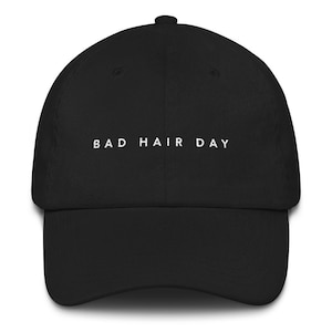 May include: A black baseball cap with white embroidered text that reads "BAD HAIR DAY".