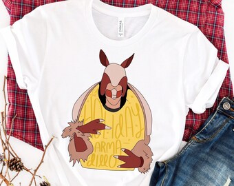 May include: White t-shirt with a cartoon illustration of a person wearing a brown and pink armadillo costume. The text "I'm the Holiday Armadillo" is written in yellow on the costume.