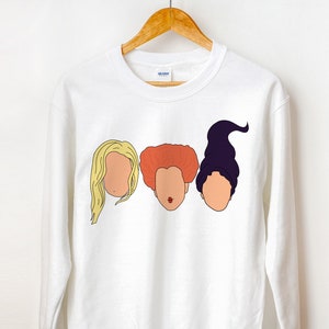 May include: White sweatshirt with a graphic of three women's faces. The faces are of the Sanderson sisters from the movie Hocus Pocus. The faces are in a row, with the blonde sister on the left, the red-haired sister in the middle, and the purple-haired sister on the right.