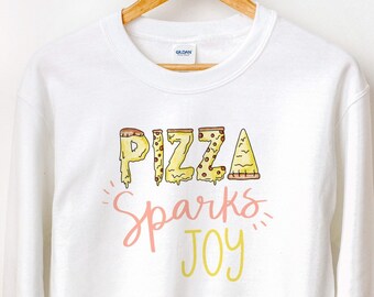 May include: White sweatshirt with a graphic design of the word "PIZZA" made of pizza slices. The text "Sparks Joy" is written below the word "PIZZA" in pink and yellow.