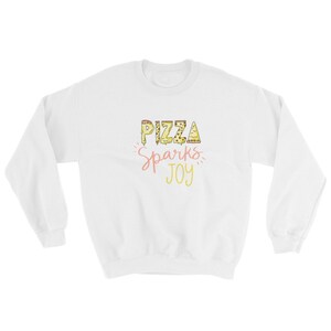 May include: White sweatshirt with the text "Pizza Sparks Joy" in yellow and pink lettering. The letters are made up of pizza slices.