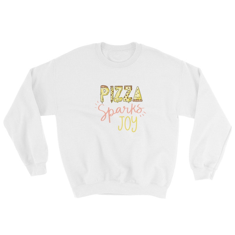 May include: White sweatshirt with the text "Pizza Sparks Joy" in yellow and pink lettering. The letters are made up of pizza slices.