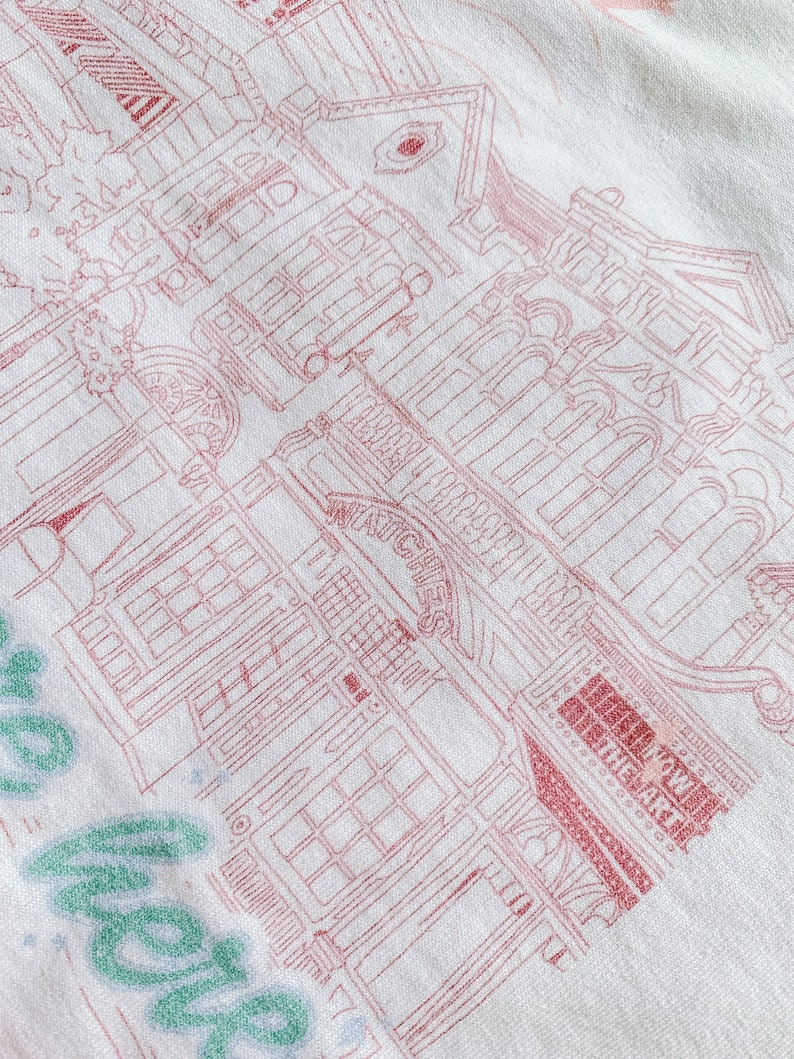 May include: A white sweatshirt with a pink outline of a building with the text "London Underground" and "The Market" on it. The text "Hello" is written in green on the bottom left corner of the sweatshirt.