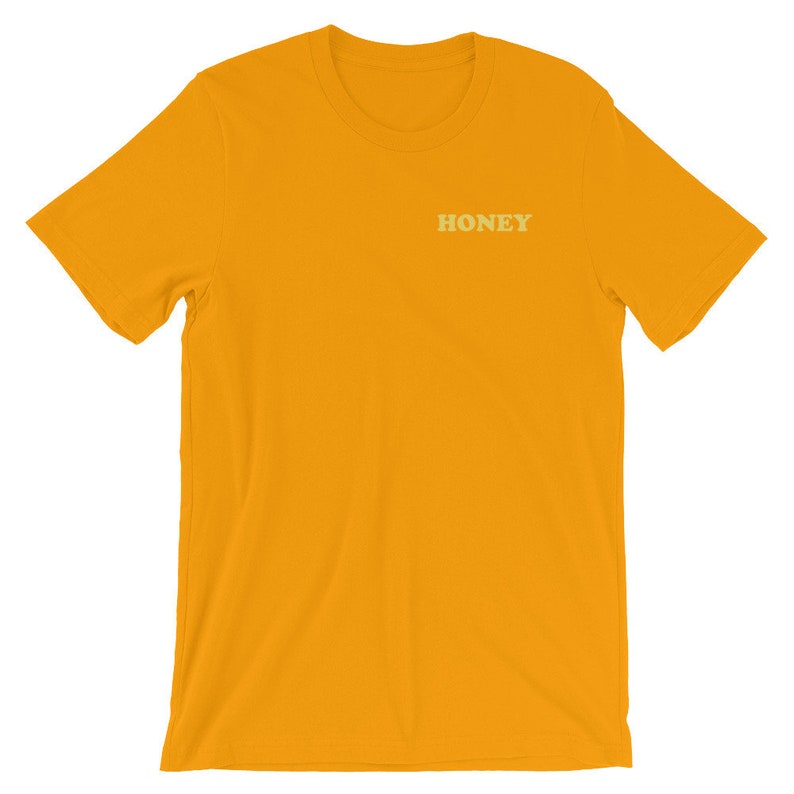 Pode incluir: Uma camiseta amarela de manga curta com a palavra "HONEY" impressa em amarelo claro na frente.