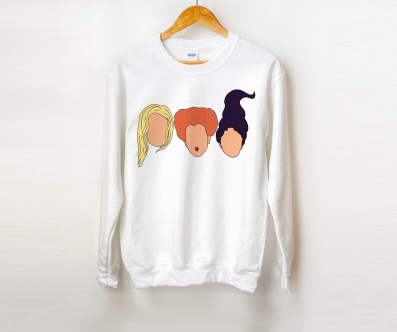 May include: White sweatshirt with a graphic of three women's faces. The faces are of the Sanderson sisters from the movie Hocus Pocus. The faces are in a row, with the blonde sister on the left, the red-haired sister in the middle, and the purple-haired sister on the right.