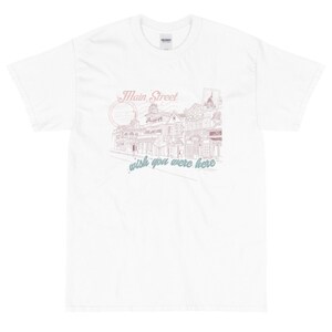May include: White t-shirt with a pink and blue graphic design of a street scene with the text "Main Street, wish you were here."