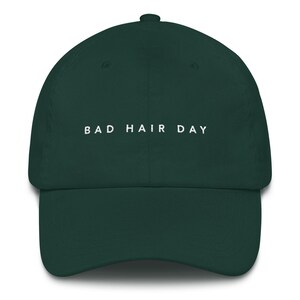 May include: A dark green baseball cap with the text "BAD HAIR DAY" embroidered in white on the front.