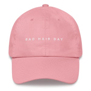 May include: A pink baseball cap with the text "BAD HAIR DAY" embroidered in white on the front.