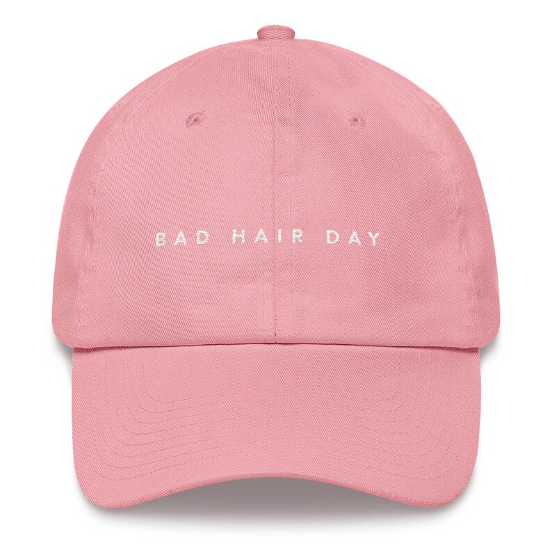 May include: A pink baseball cap with the text "BAD HAIR DAY" embroidered in white on the front.