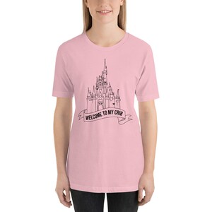 May include: A pink t-shirt with a black outline of Cinderella's castle and the text "Welcome to my crib" on a banner.