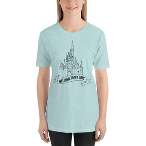 May include: A light blue t-shirt with a black outline of a castle and the text "WELCOME TO MY CRIB" on a banner.