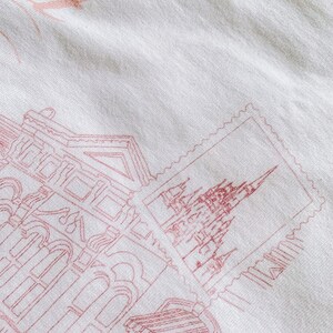 May include: A white fabric tote bag with a pink outline of a building and a stamp with a pink outline of a castle. The text "Book" is printed in pink on the bag.