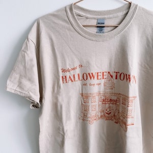 May include: A beige t-shirt with a red graphic print of a building with the text "Welcome to... HALLOWEEN TOWN est. long ago CITY HALL"