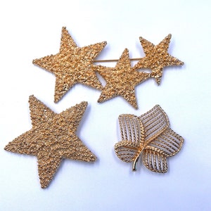 May include: A set of four gold-tone brooches featuring a leaf and three star shapes. The brooches are made of textured metal.