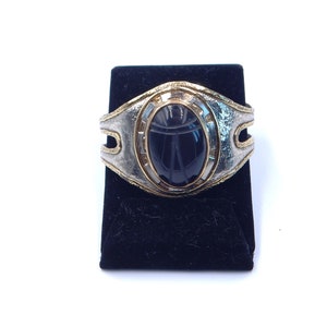 May include: A silver and gold bracelet with a black scarab beetle design. The beetle is carved into a black stone and set in a silver and gold frame.